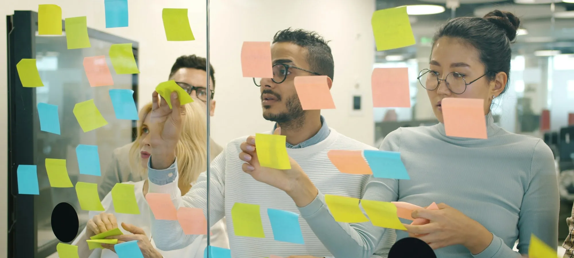 Three people working through sticky notes on a glass wall in a workshop