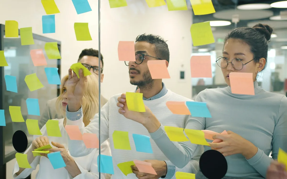 Three people working through sticky notes on a glass wall in a workshop