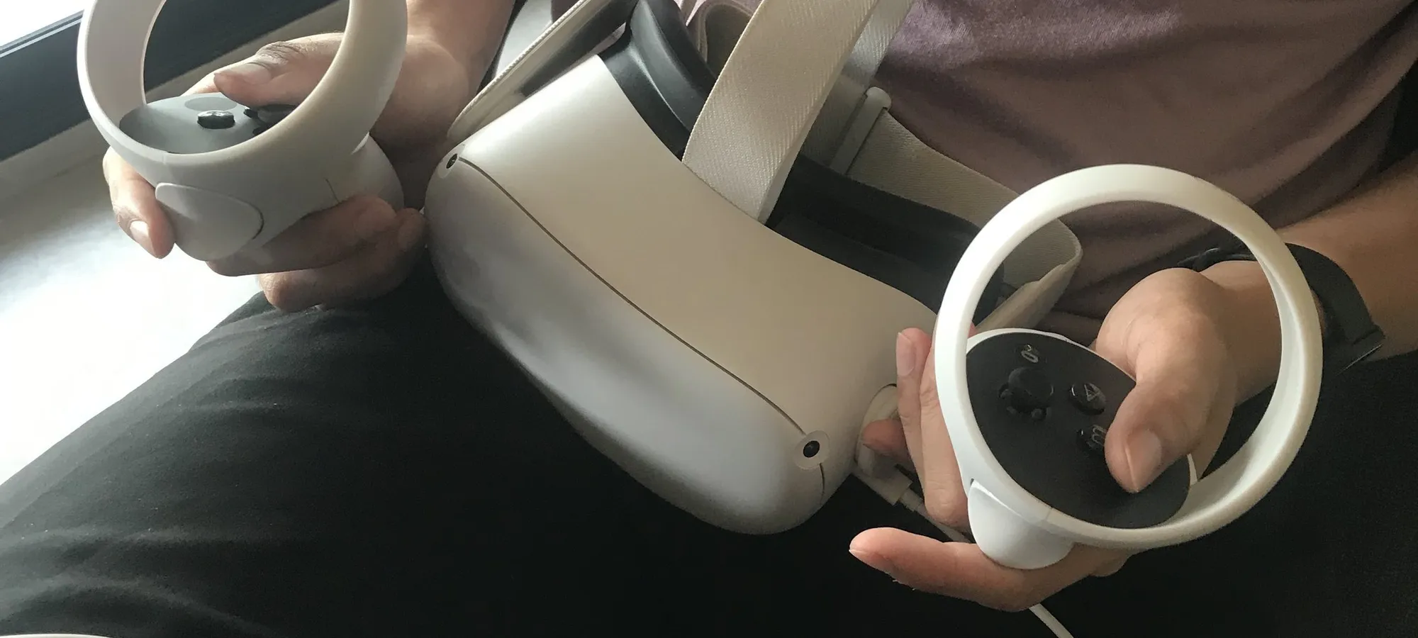 Hands holding a white virtual reality headset and its two controllers