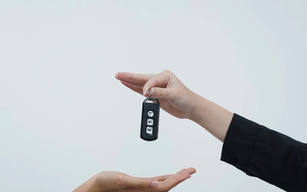 One hand passing a car key to another against a pale grey background