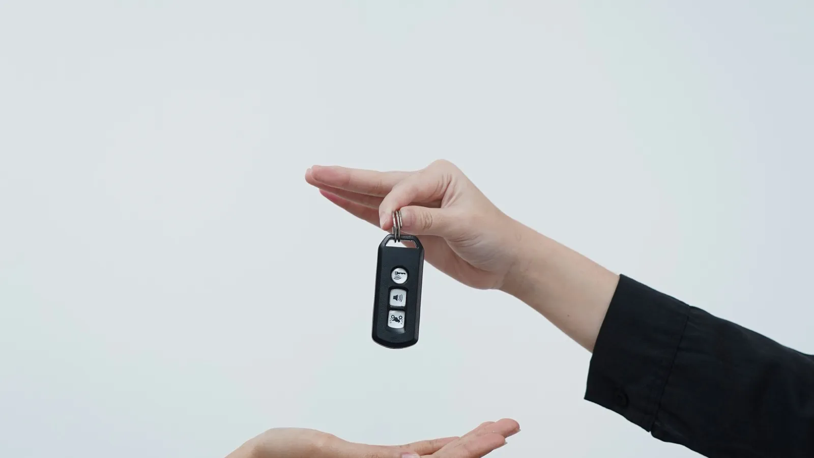 One hand passing a car key to another against a pale grey background